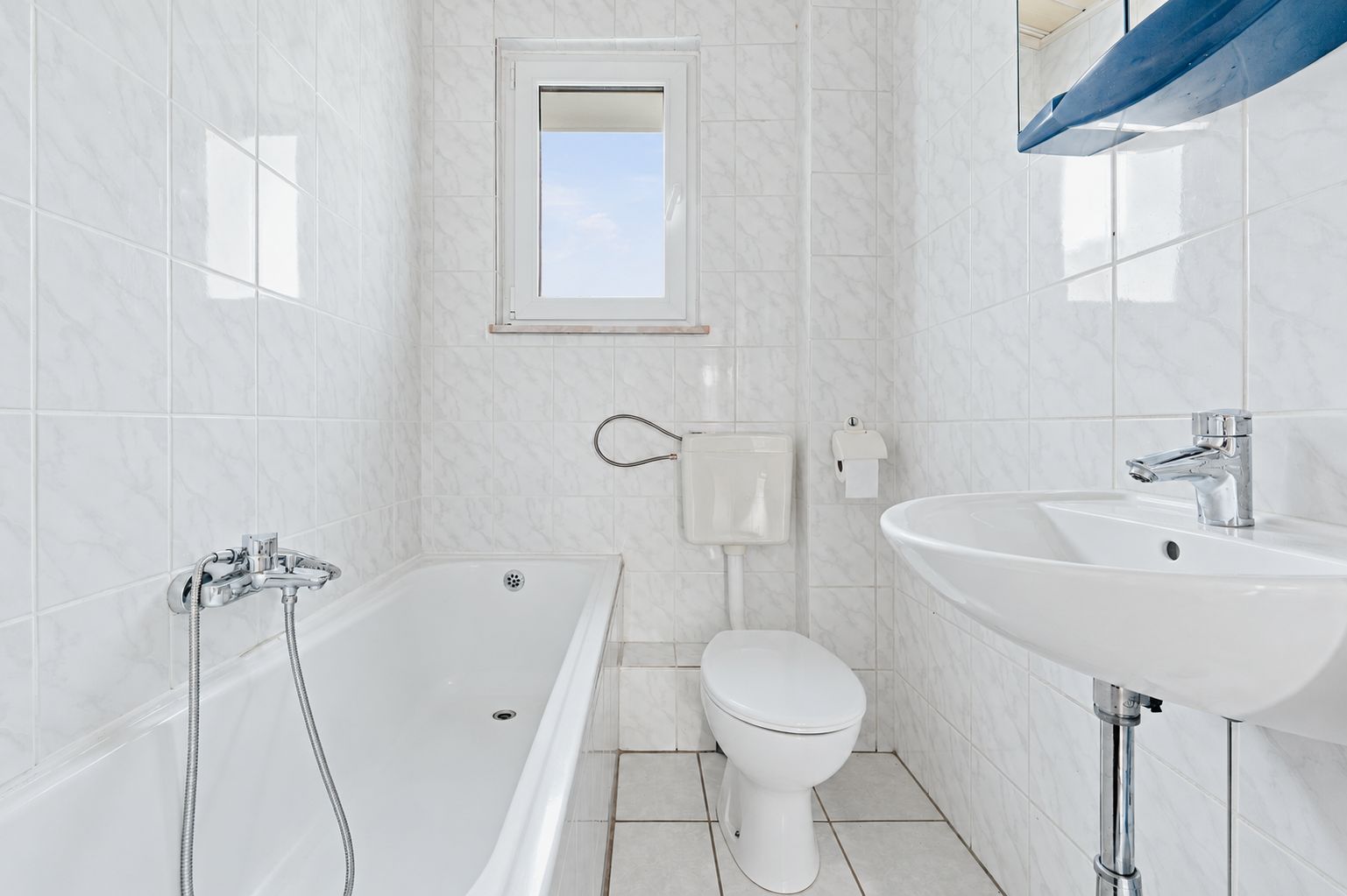 Helles Badezimmer mit Badewanne, Toilette, Waschbecken und Fenster.