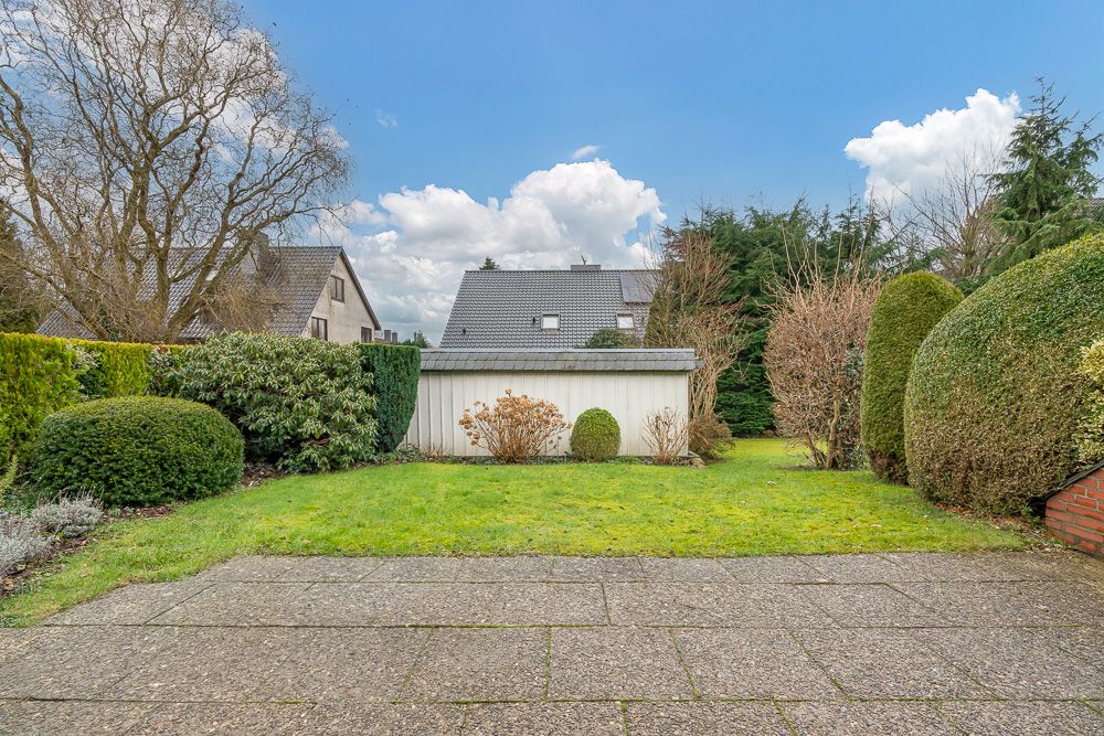 Gepflegter Garten mit Rasenfläche, Sträuchern und einer weißen Garage im Hintergrund.