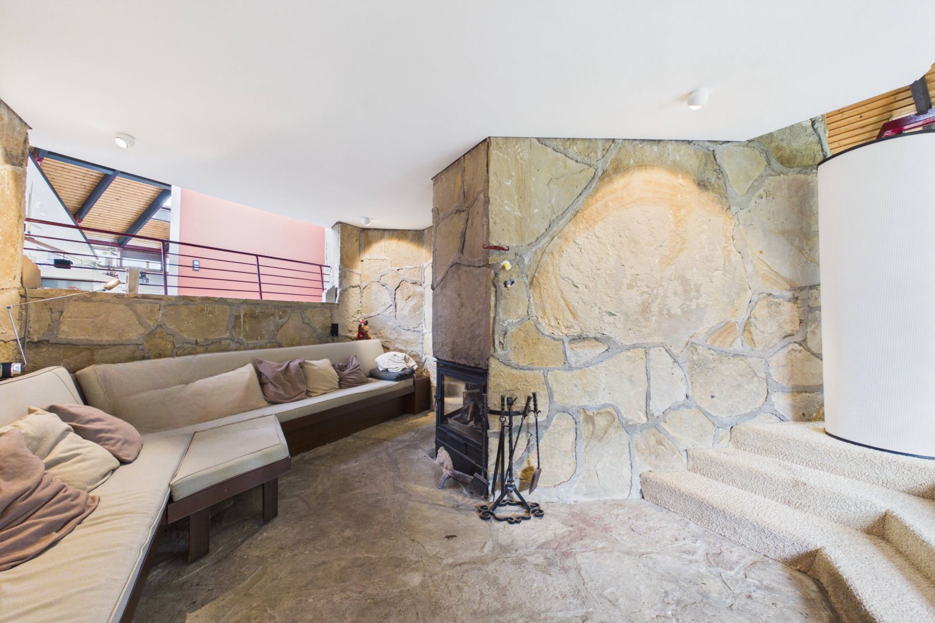 Wohnraum mit gemauerter Steinwand, Kamin, beigen Sofas und Treppe.