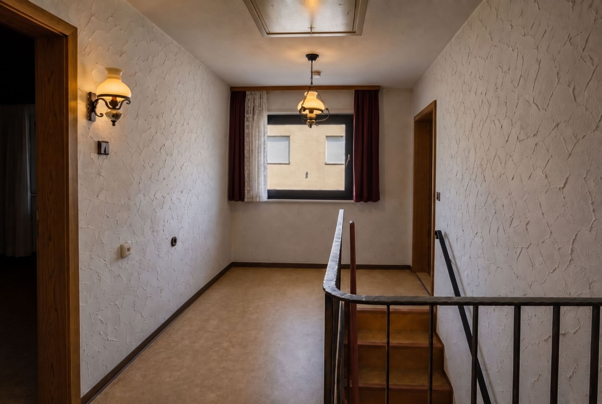 Flur mit Treppe, Fenster, Wandlampen und zwei offenen Türen in einer Wohnimmobilie.