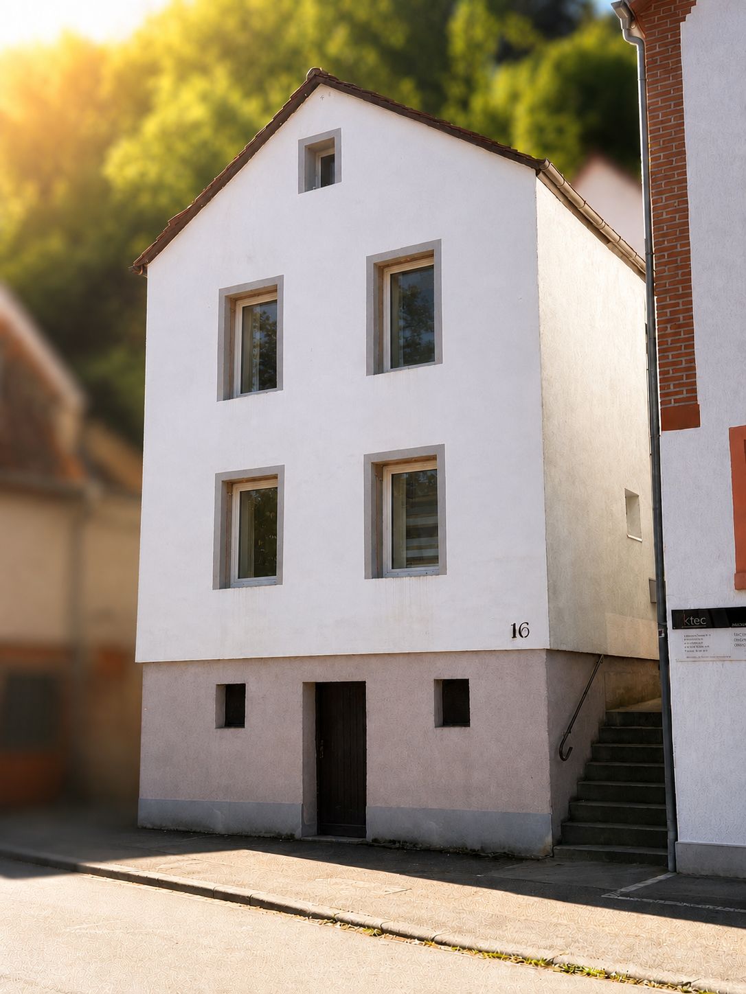 Weißes, dreistöckiges Wohnhaus mit Treppe an der Seite und fünf Fenstern zur Straße.