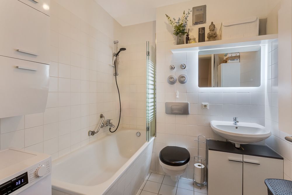 Modernes Bad mit Badewanne, Waschbecken, wandhängender Toilette und beleuchtetem Spiegel.