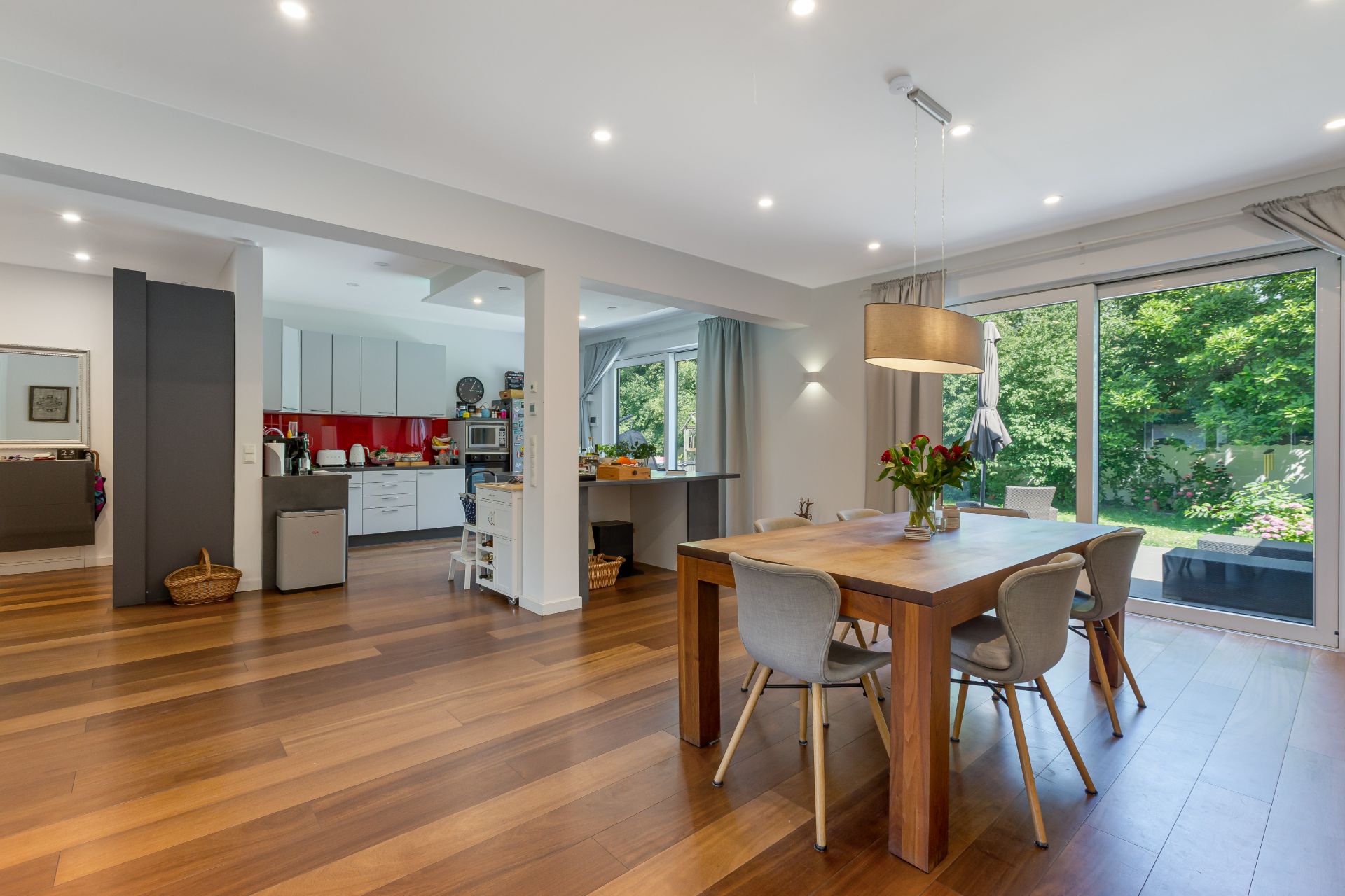 Helles Esszimmer mit Holzboden, großem Tisch und Blick in eine moderne Küche, Fenster zum Garten.