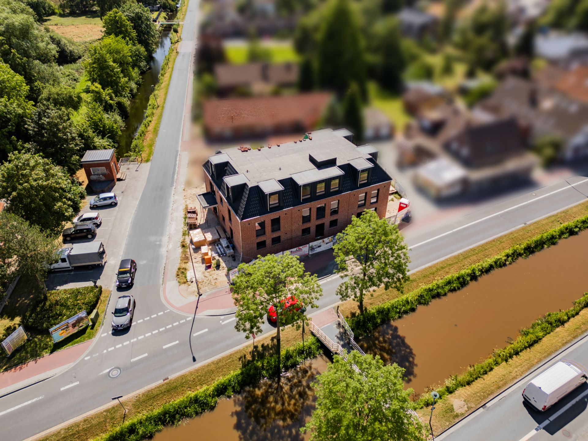 Luftaufnahme eines modernen Wohngebäudes an einer Straße mit Kanal und Bäumen.