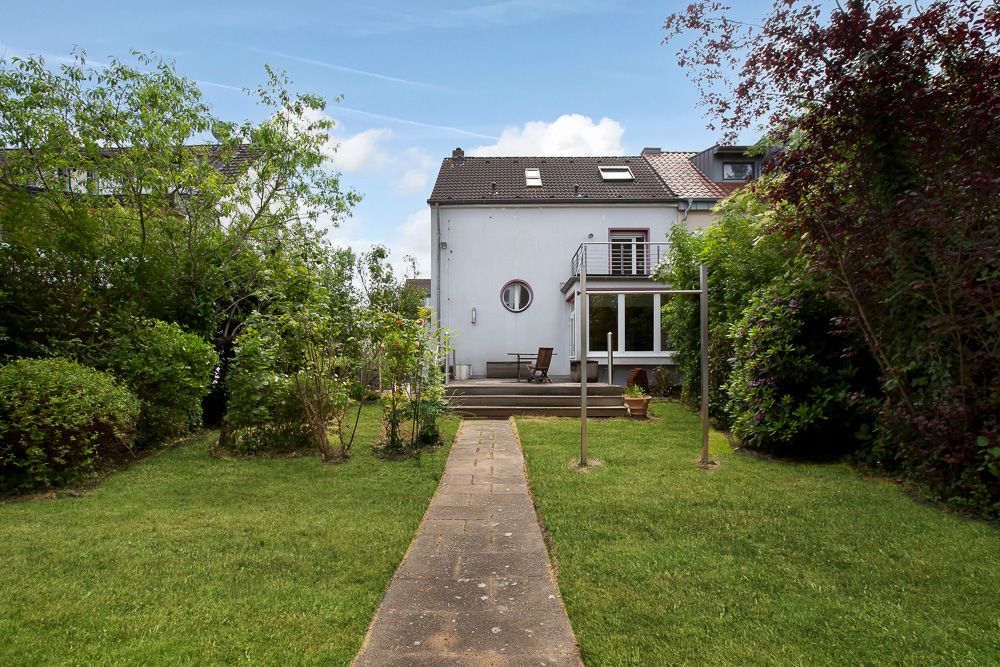 Gepflegter Garten mit Weg und Terrasse hinter einem weißen Wohnhaus.