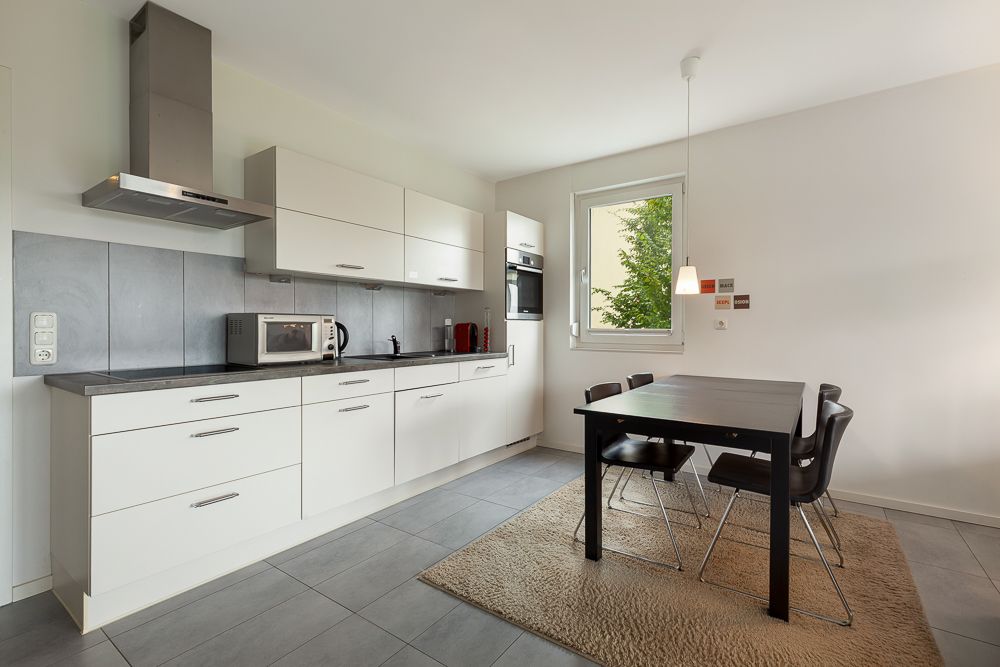 Moderne Einbauküche mit Esstisch, vier Stühlen und großem Fenster auf einem hellen Teppich.