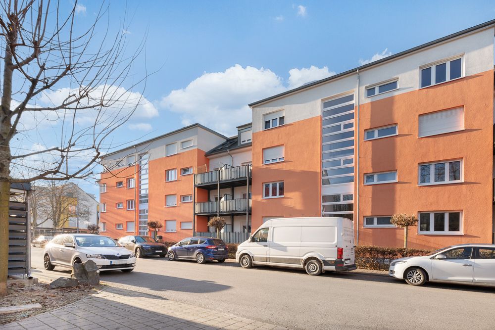 Wohnhaus mit orangefarbener Fassade, mehreren Balkonen und parkenden Autos auf der Straße.
