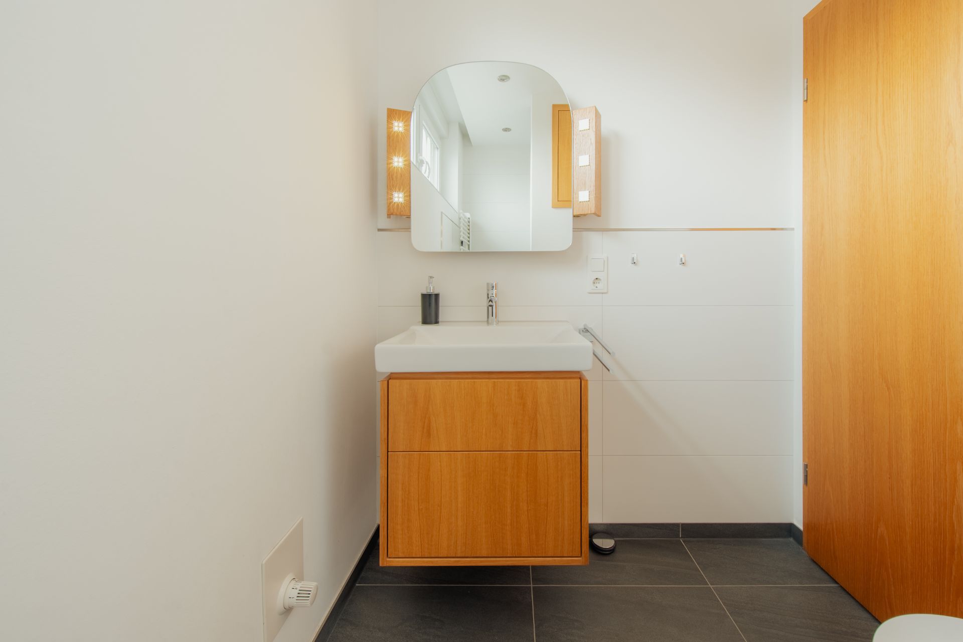 Modernes Badezimmer mit Waschbecken, Holzunterschrank und beleuchtetem Spiegel.