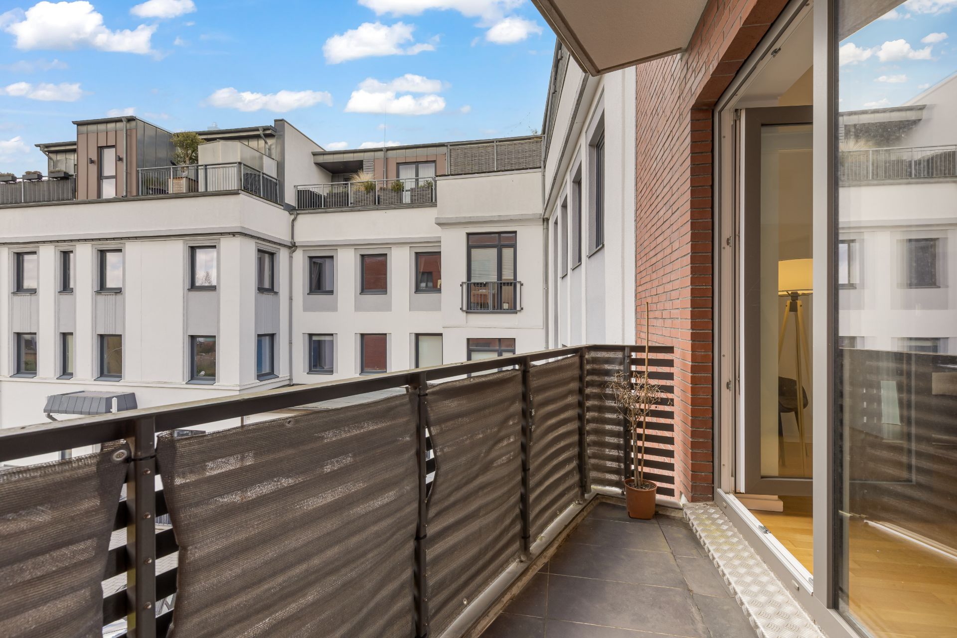 Moderner Balkon mit Blick auf benachbarte Wohngebäude, Zugang durch eine große Glasschiebetür.
