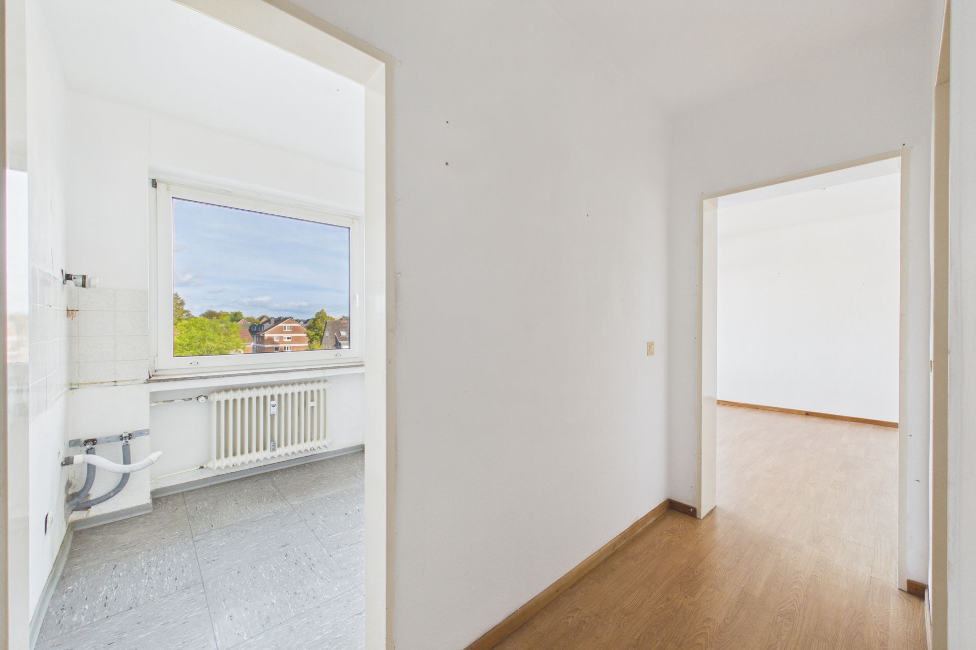Flur mit Blick in eine Küche mit Fenster und ein Zimmer mit Holzboden.