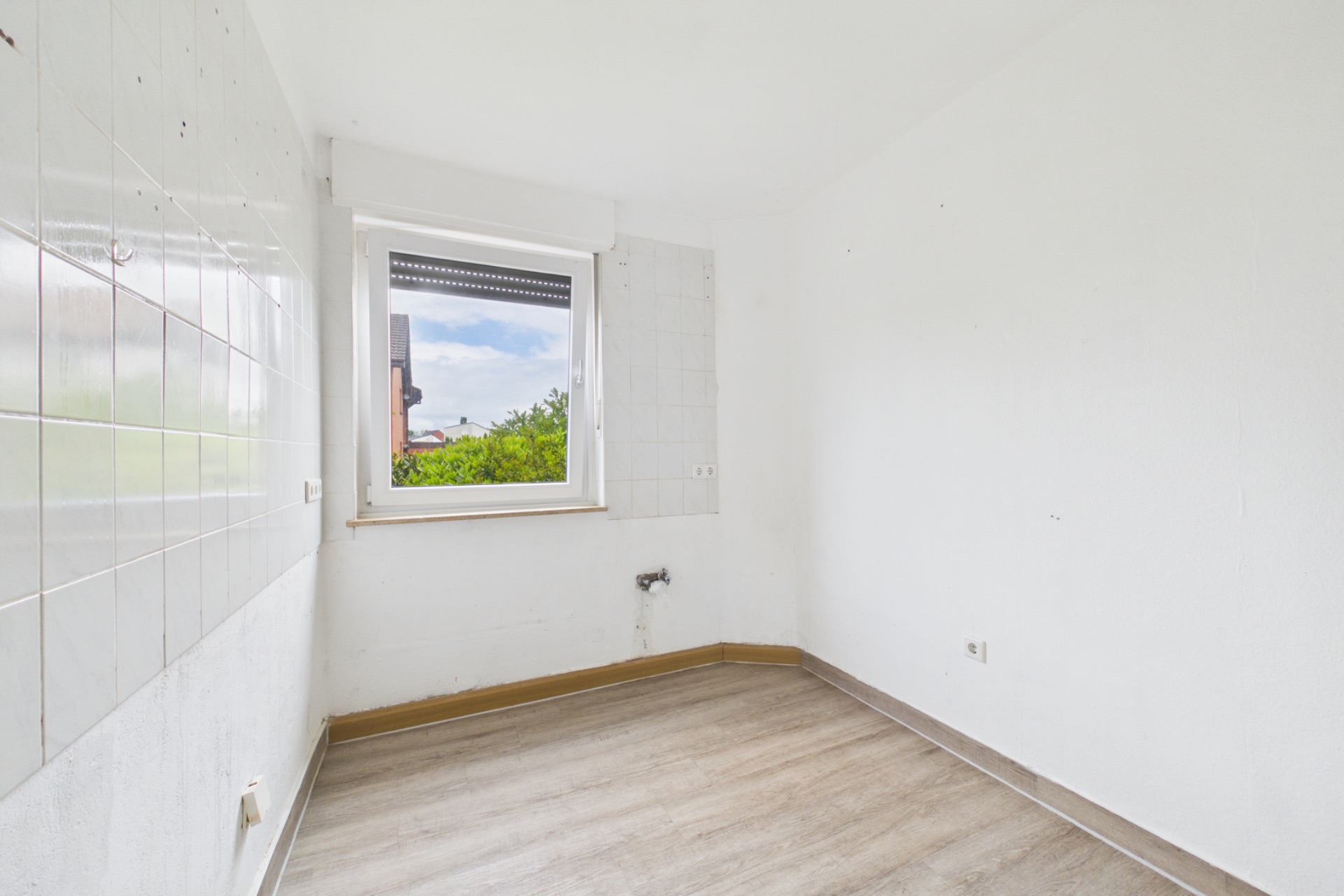 Leerer, kleiner Raum mit weiß gestrichenen Wänden, Fenster und Fliesen an einer Wand.