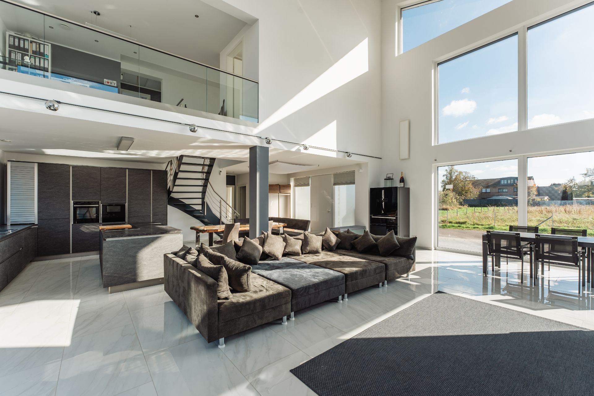 Modernes Wohnzimmer mit großer Couch, Esstisch, offener Küche und großer Fensterfront.