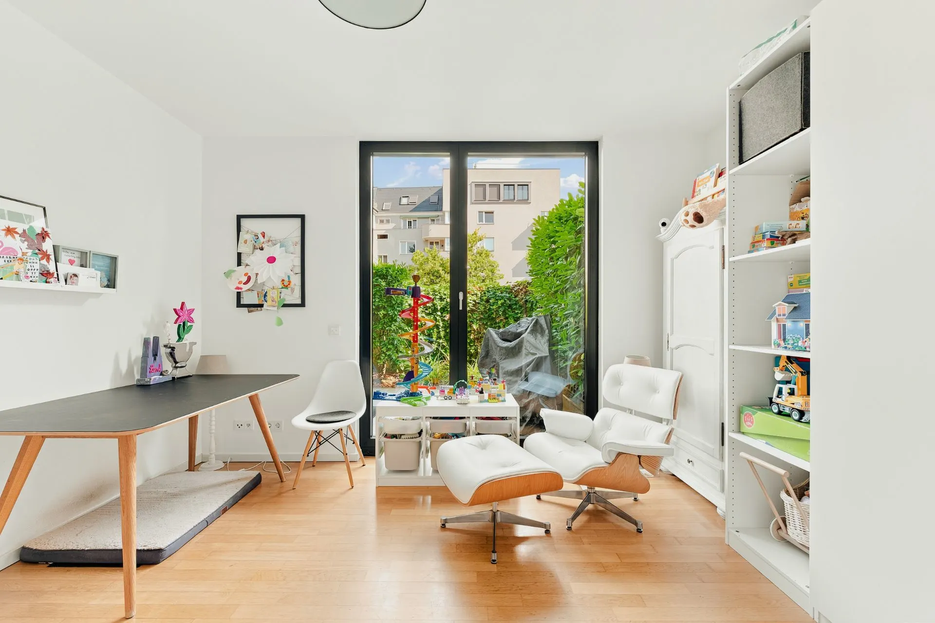Helles Zimmer mit Schreibtisch, Regal, Sessel und Fenster zum Garten.