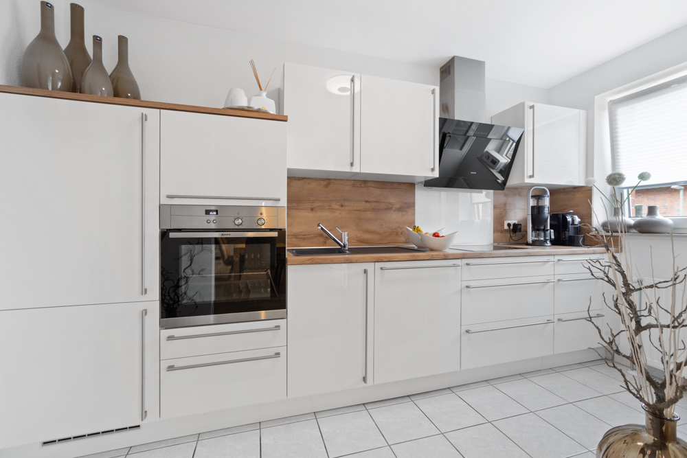 Moderne weiße Küche mit Holzarbeitsplatte, Backofen, Spüle und Kaffeemaschine.