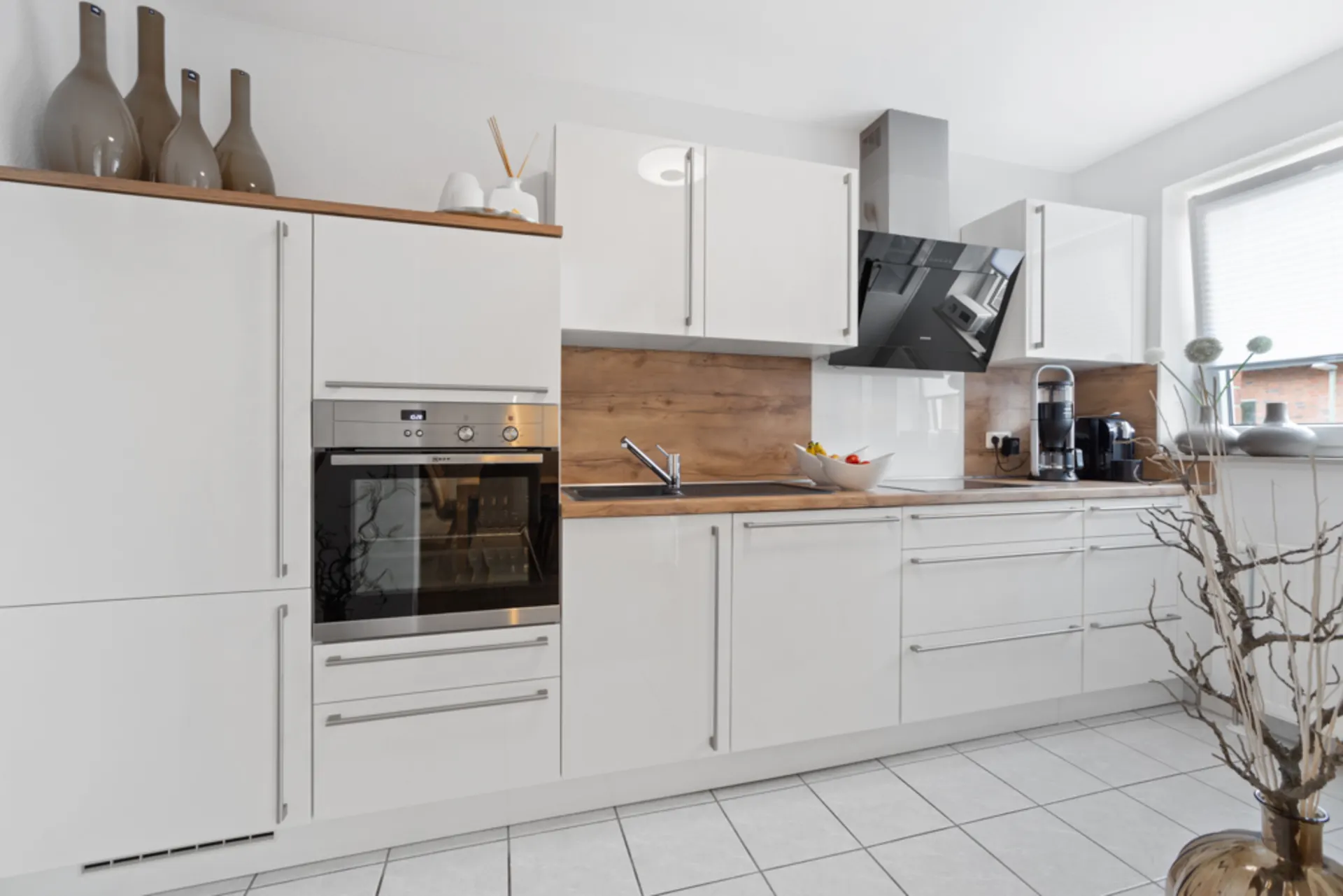 Moderne weiße Küche mit Holzarbeitsplatte, Backofen, Spüle und Kaffeemaschine.