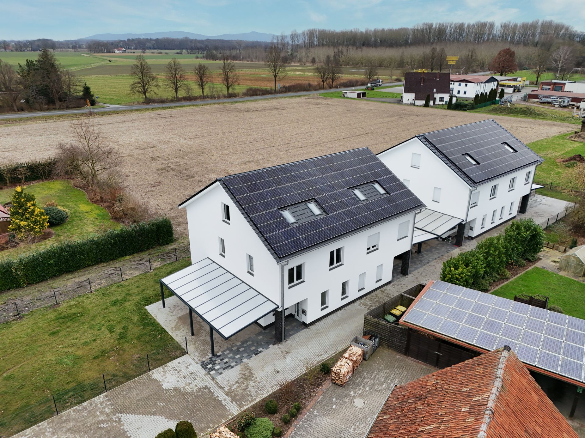Zwei weiße Wohnhäuser mit Solaranlagen auf den Dächern neben Feldern und Wiesen.