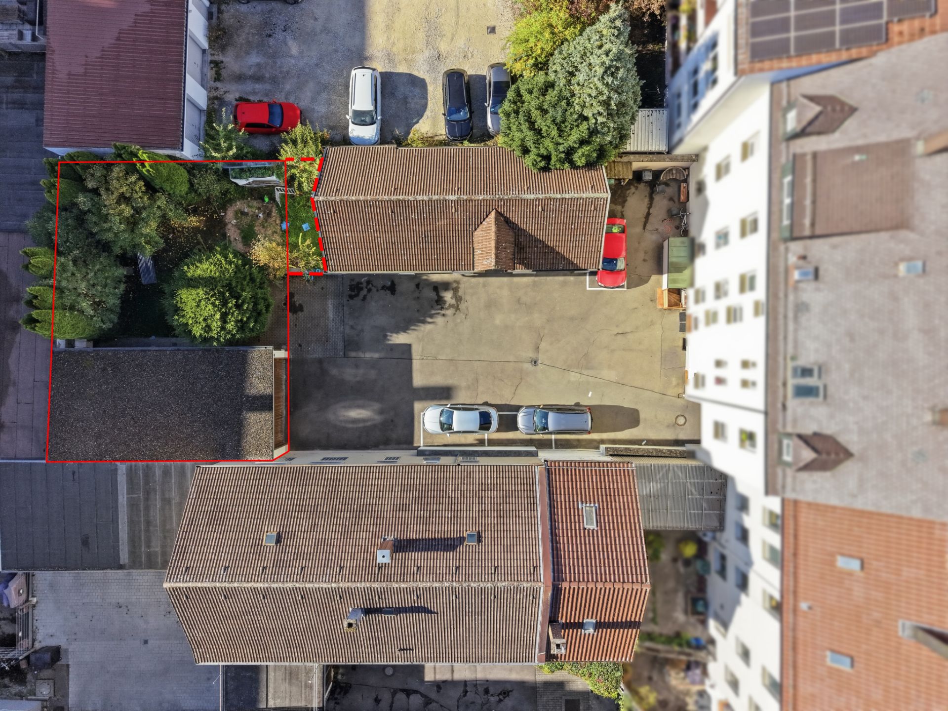 Luftaufnahme eines Innenhofs mit geparkten Autos, Gebäuden und einem begrünten Bereich.