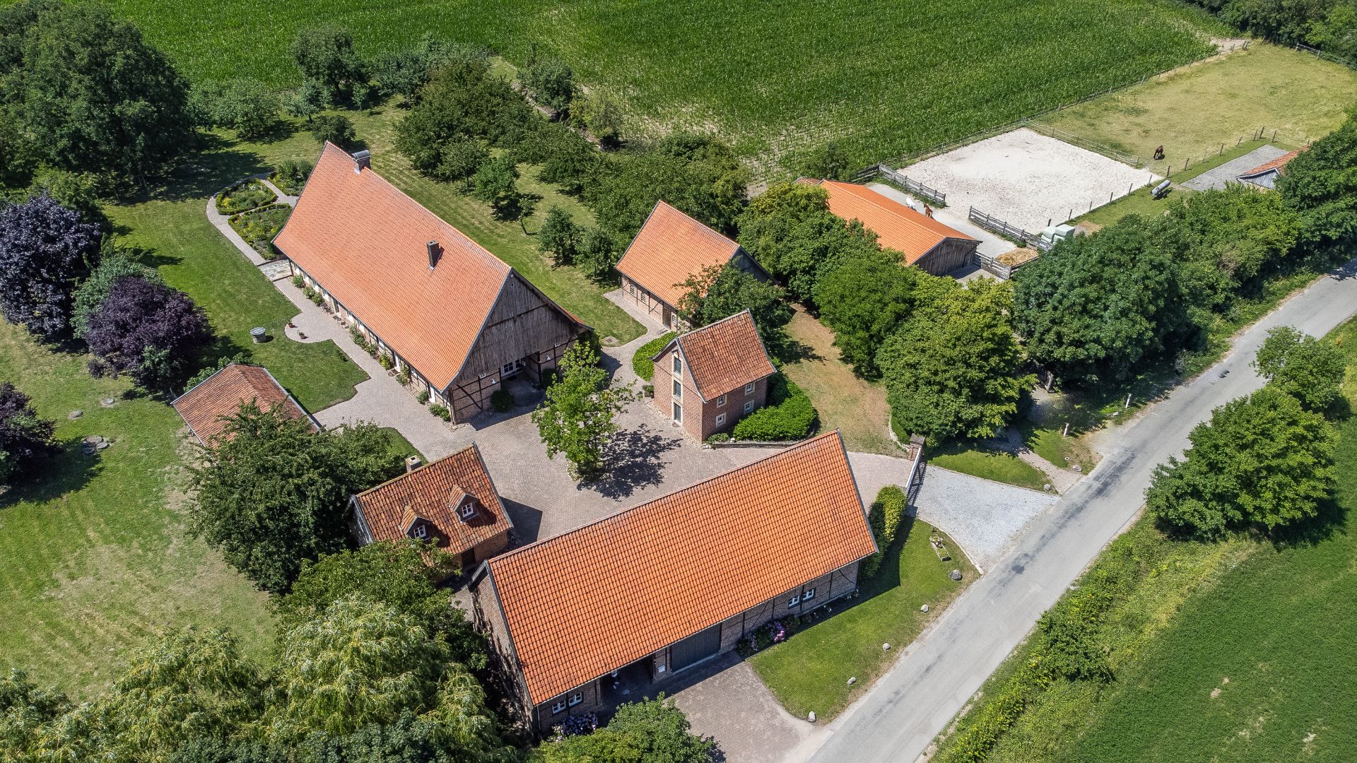 Luftaufnahme eines Bauernhofs mit mehreren Gebäuden, roten Dächern und umgebenden Feldern.
