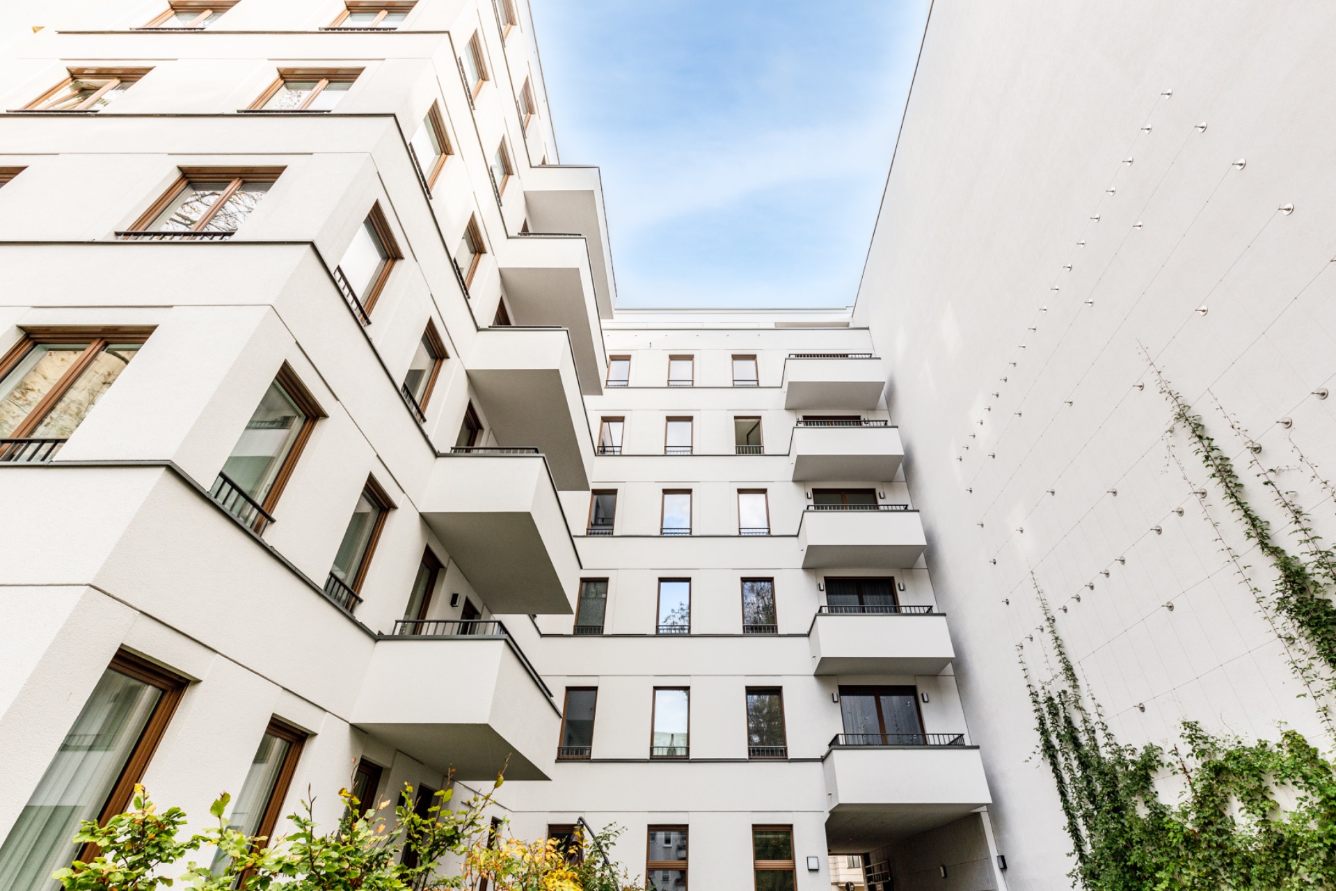 Moderne Wohnhausfassade mit mehreren Balkonen und Pflanzen an der Wand im Innenhof.