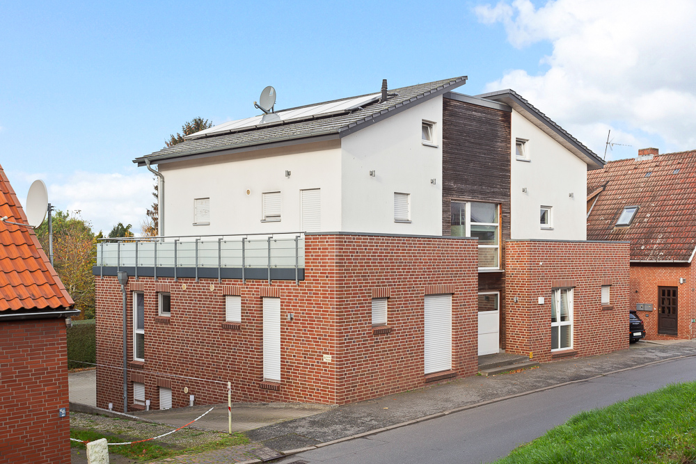Modernes Wohnhaus mit roter Klinkerfassade und großer Terrasse, an einer Straße gelegen.