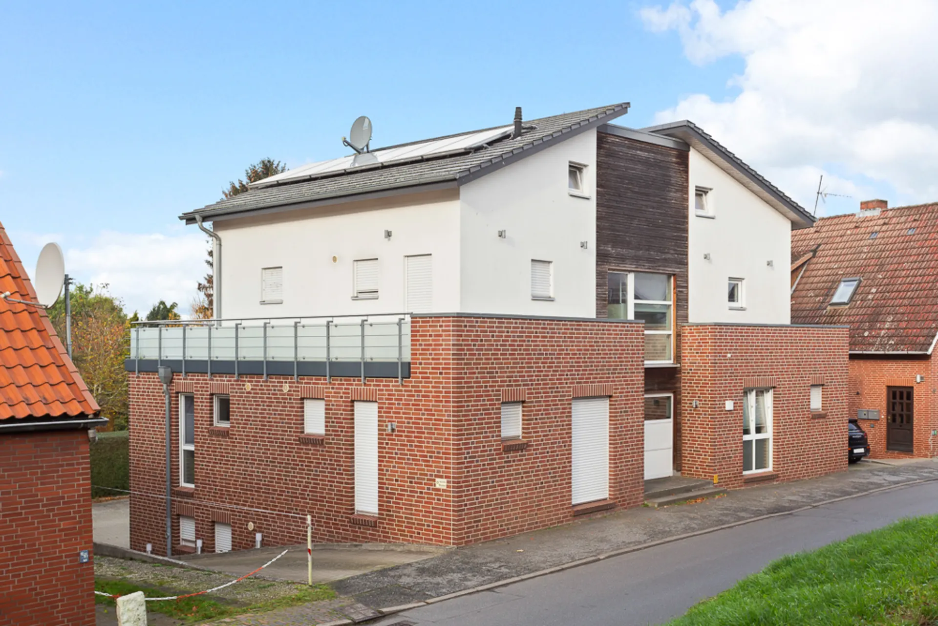 Modernes Wohnhaus mit roter Klinkerfassade und großer Terrasse, an einer Straße gelegen.