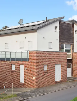 Modernes Wohnhaus mit roter Klinkerfassade und großer Terrasse, an einer Straße gelegen.