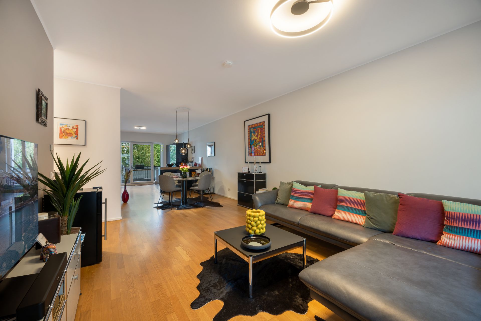 Modernes Wohnzimmer mit Ecksofa, Couchtisch und Blick auf Essbereich mit Holzboden.