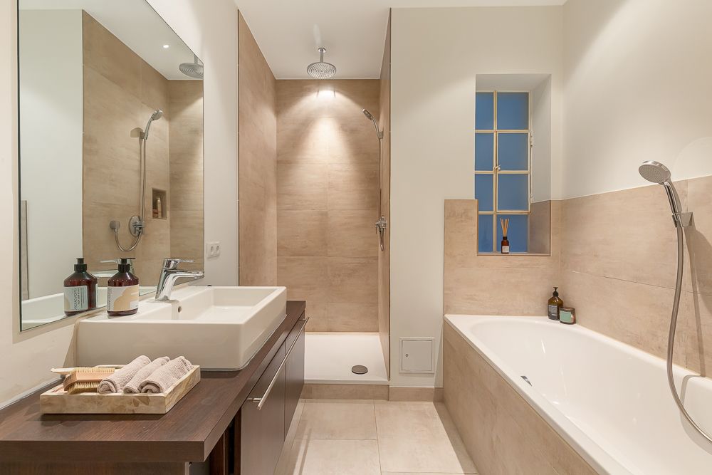 Modernes Badezimmer mit Waschbecken, Dusche und Badewanne, helle Fliesen und Fenster.
