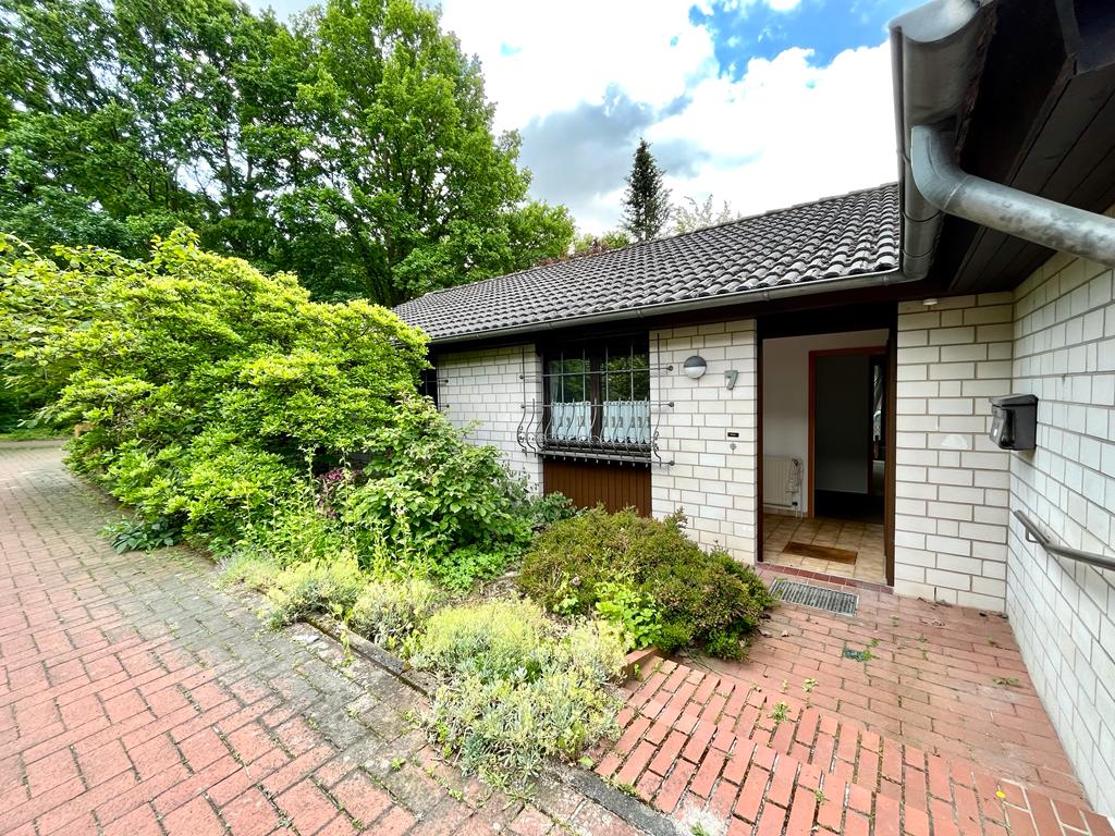 Eingang eines Hauses mit hellem Mauerwerk, roten Ziegelsteinen und umgeben von Sträuchern.