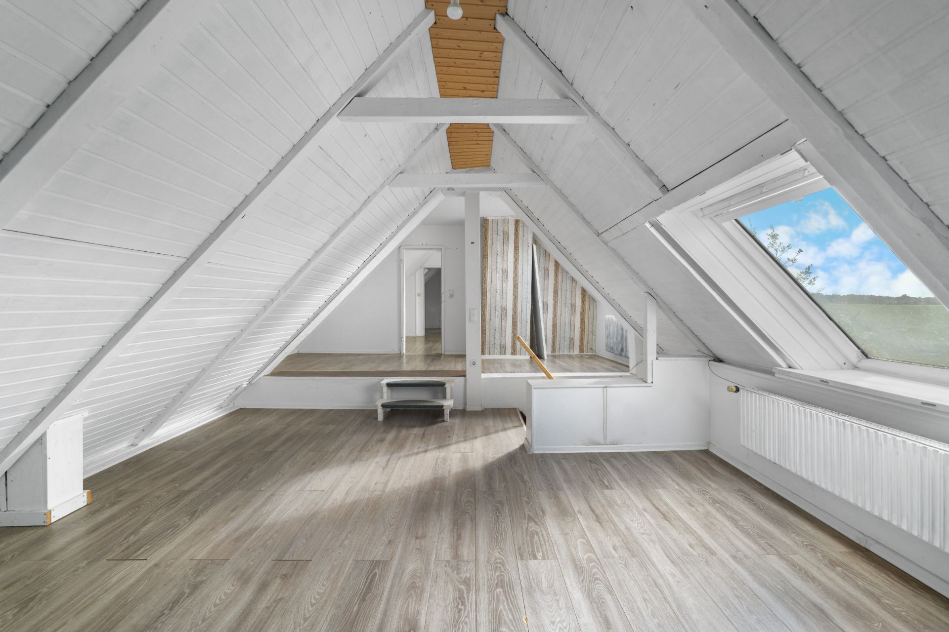Heller Dachbodenraum mit schrägen Wänden, großem Fenster und Holzfußboden.