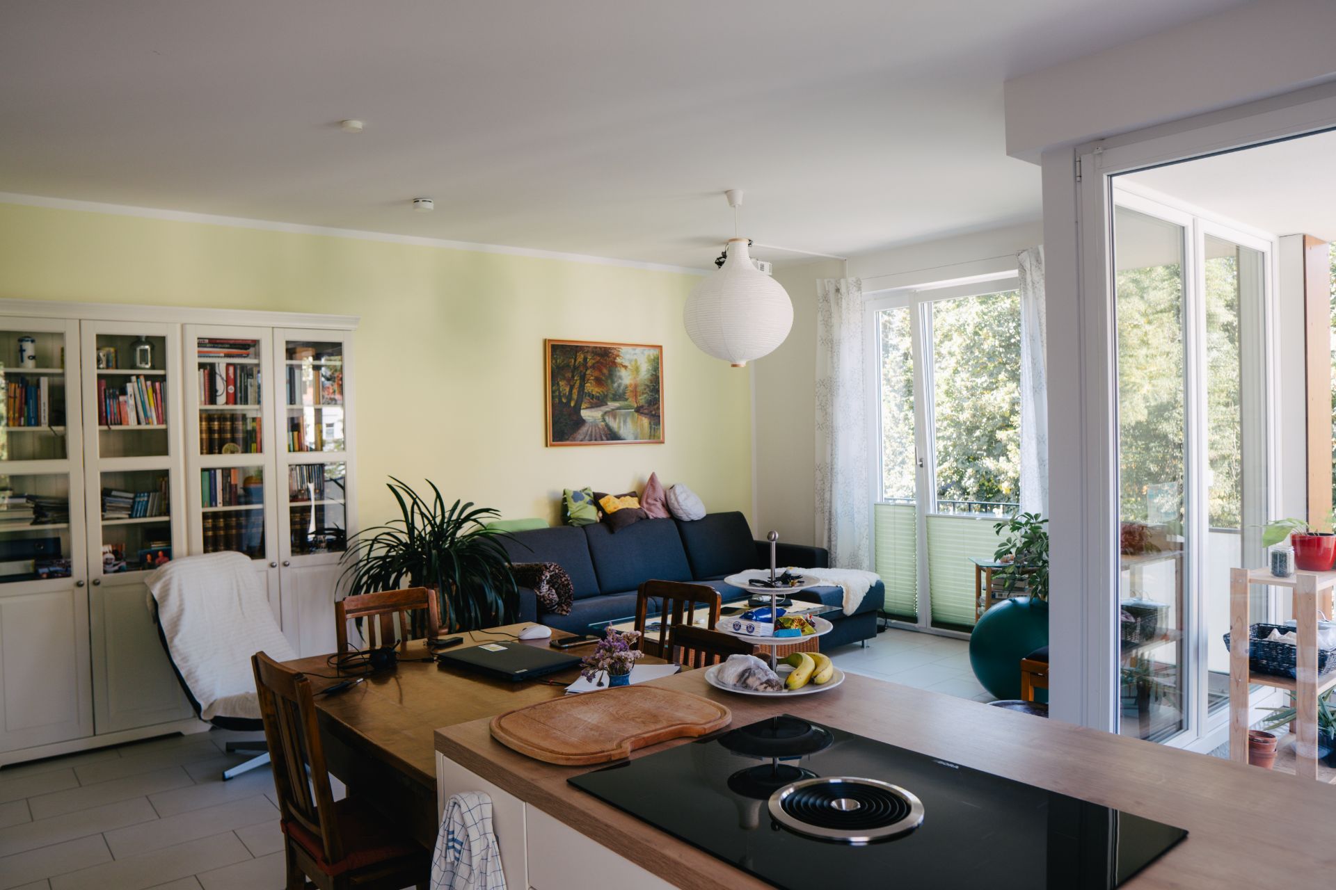Helles Wohnzimmer mit Sofa, Esstisch, Bücherregal und Zugang zu einem Balkon.