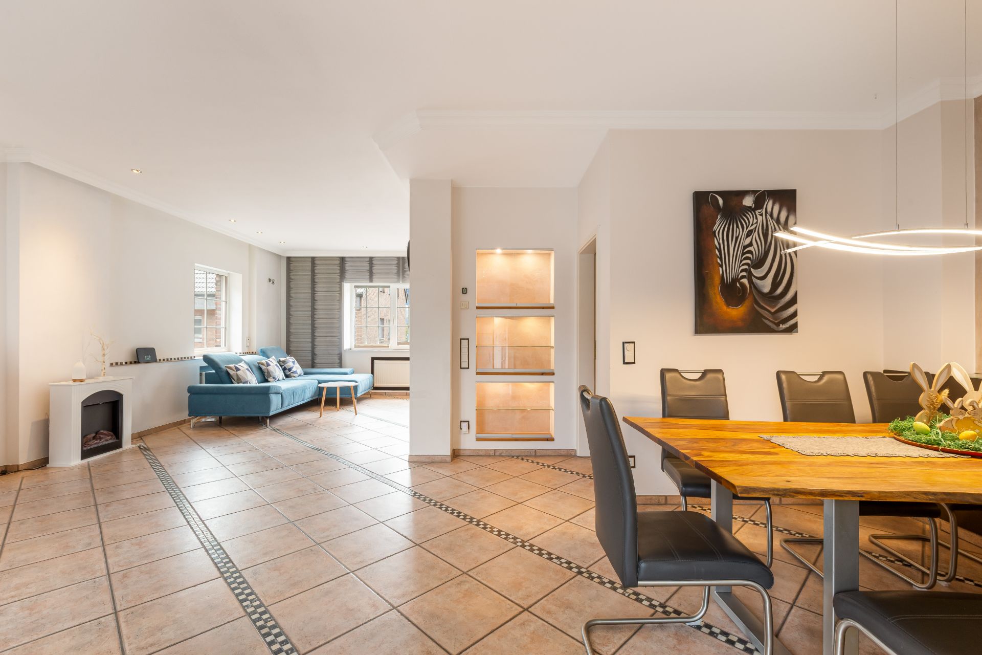 Helles Wohnzimmer mit blauer Couch, Essbereich und einem Zebrabild an der Wand.