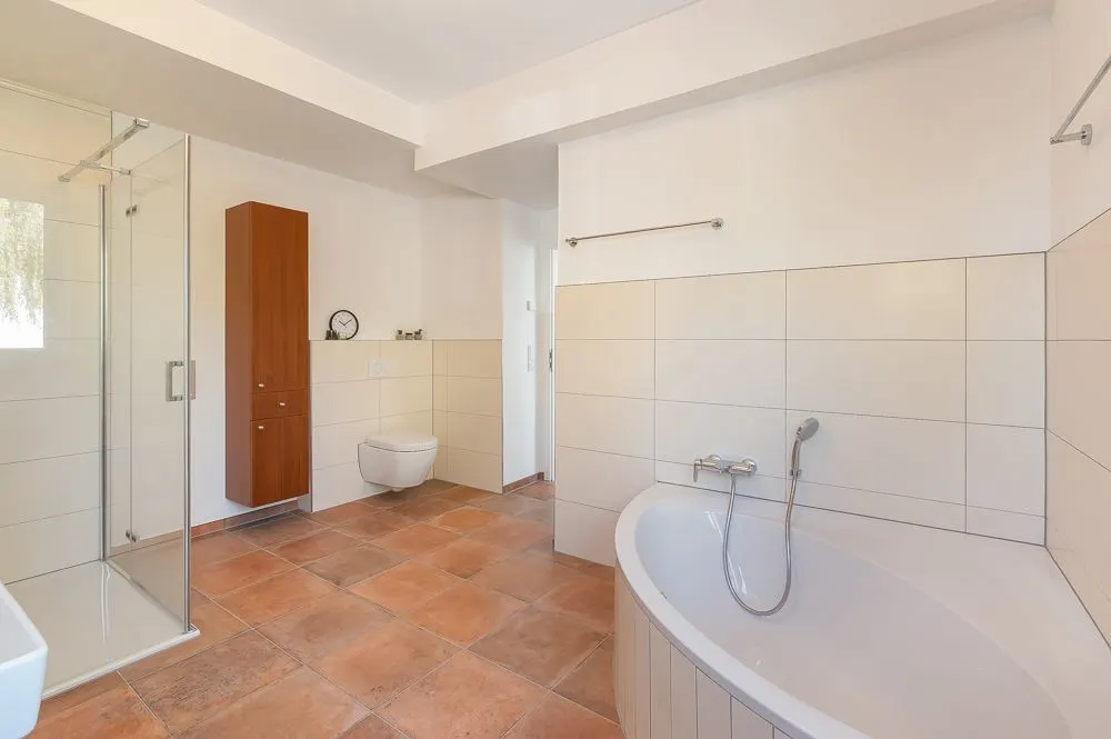 Modernes Badezimmer mit Dusche, Badewanne, WC, Schrank und beigen Fliesen.