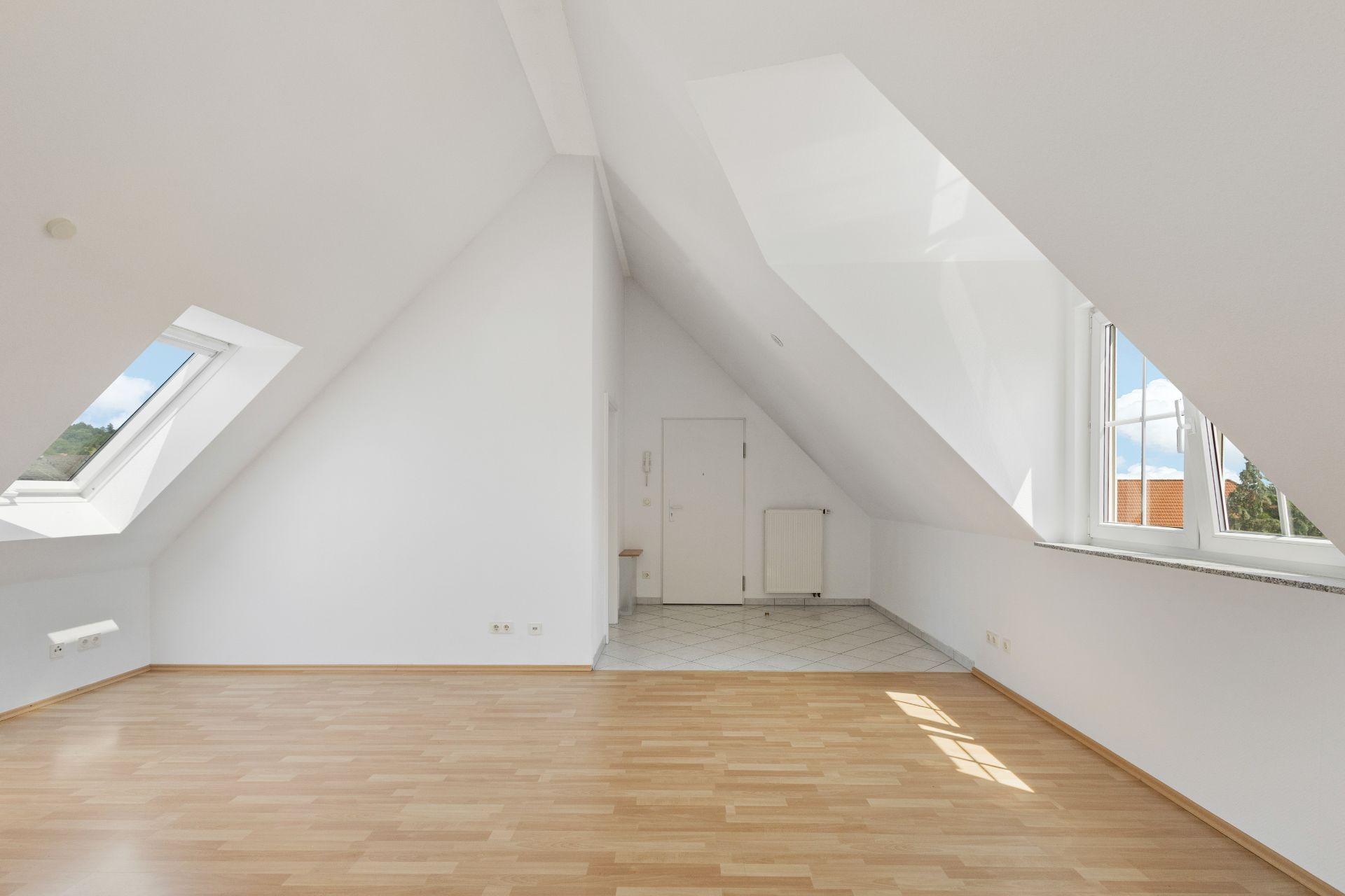 Helles Dachzimmer mit schrägen Decken, Laminatboden und zwei Fenstern.