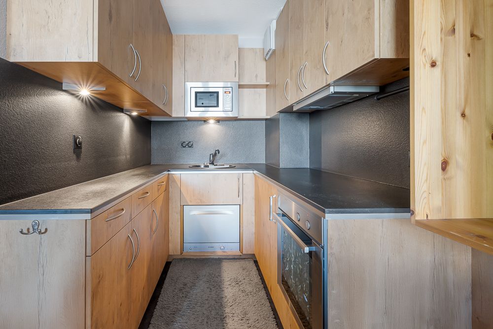 Moderne Einbauküche mit Holzfronten, schwarzer Arbeitsplatte, Backofen und Mikrowelle.