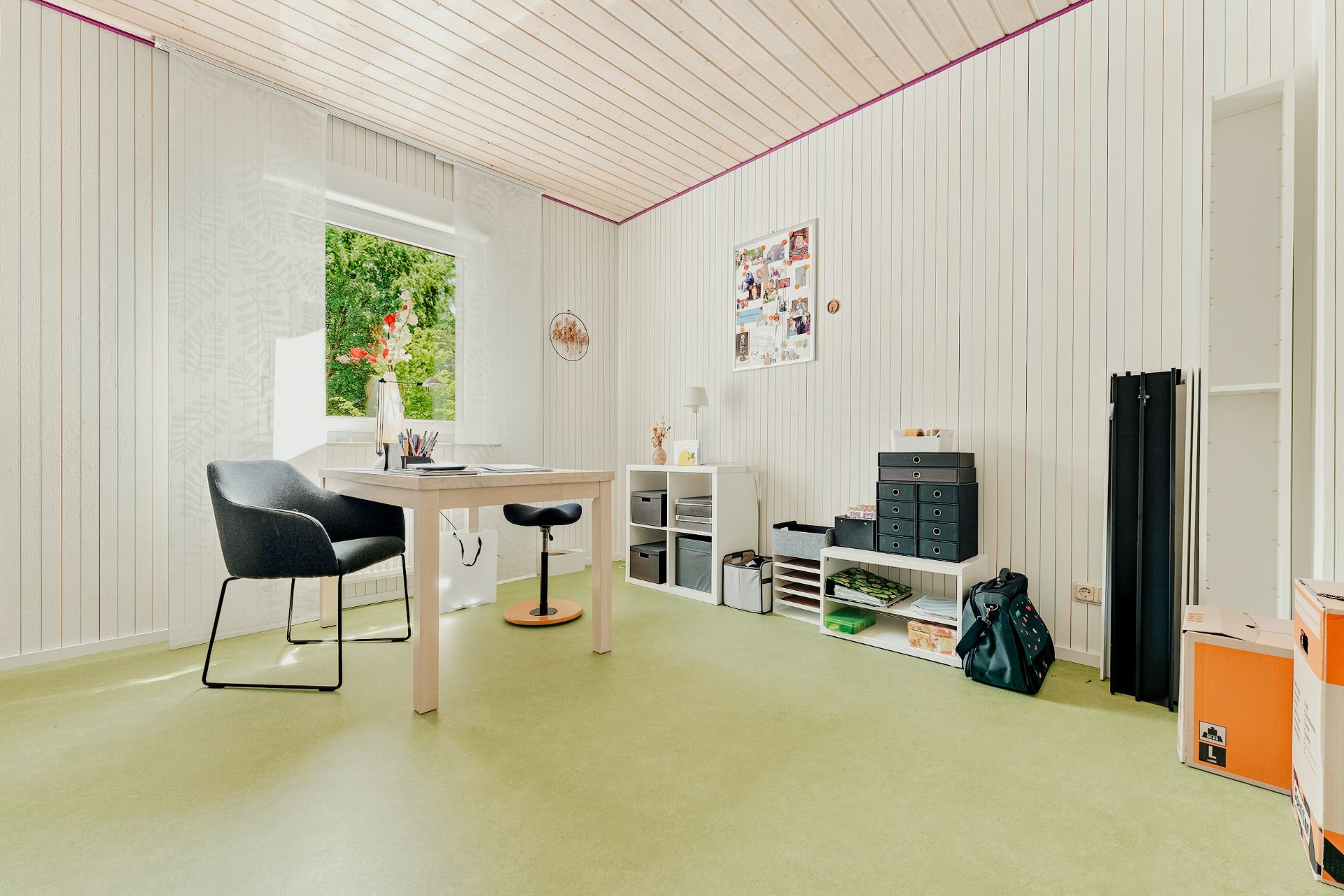 Helles Arbeitszimmer mit Schreibtisch, zwei Stühlen, Regal, Fenster und Dekoration an der Wand.