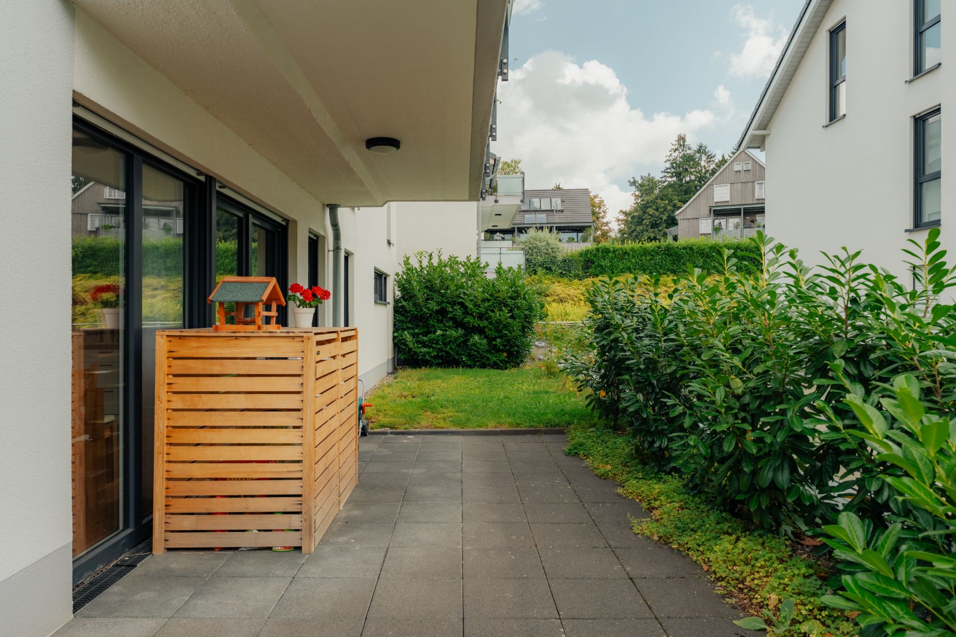 Gepflasterte Terrasse mit Holzzaun und Blick auf Garten und angrenzende Wohnhäuser.