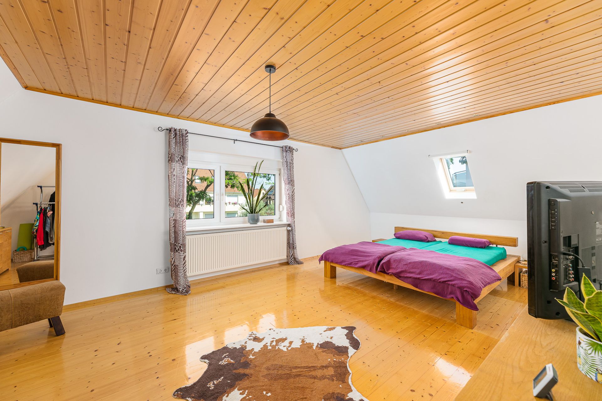 Helles Schlafzimmer mit Holzdecke, Doppelbett, großem Fenster und Fernseher.
