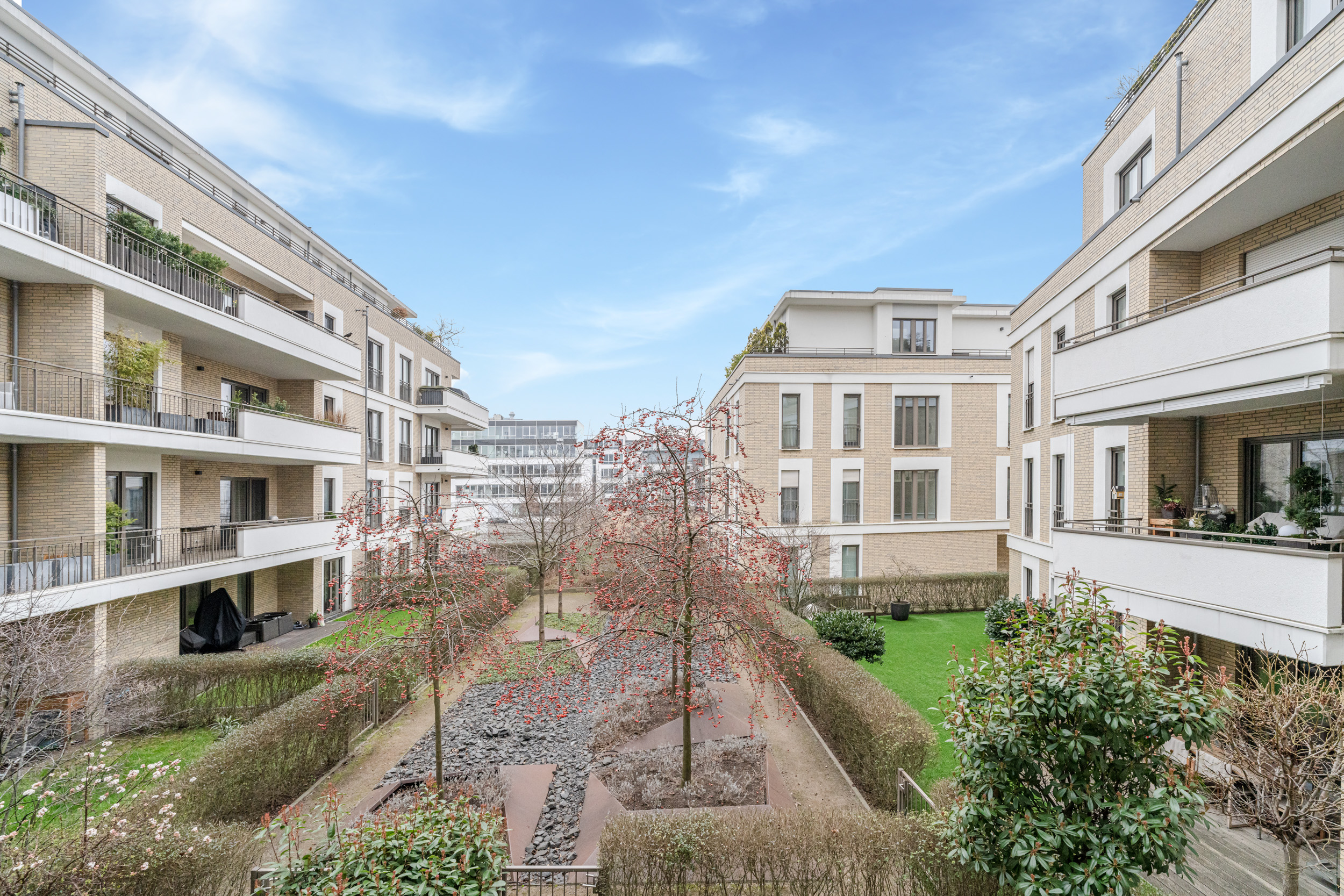 Moderner Innenhof mit Grünflächen, Bäumen und mehreren Wohnhäusern mit Balkonen.