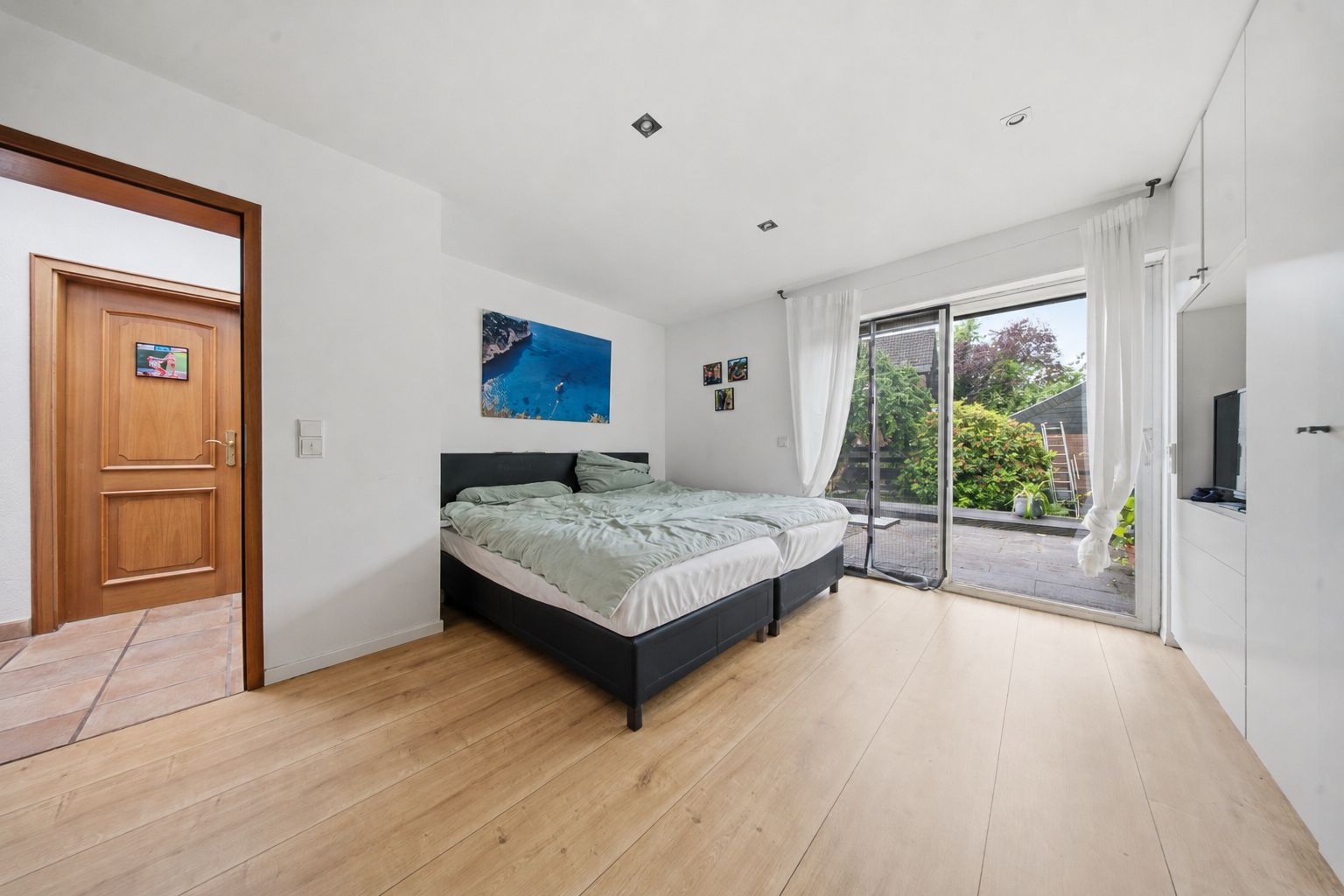 Helles Schlafzimmer mit Doppelbett, Holzfußboden und Zugang zur Terrasse durch Glastür.