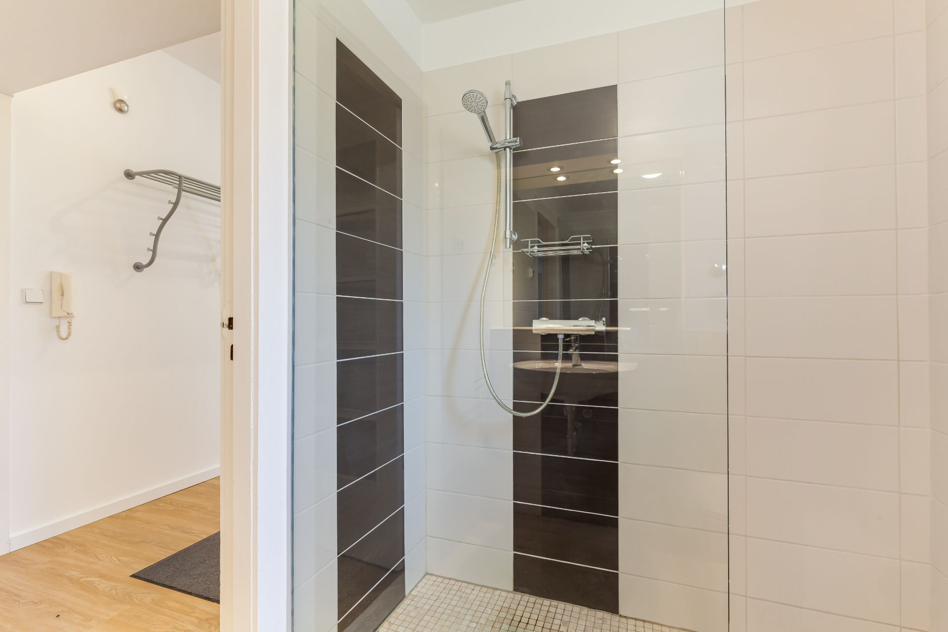 Moderne, offene Dusche mit dunklen und hellen Fliesen, daneben ein Eingangsbereich mit Holzboden.