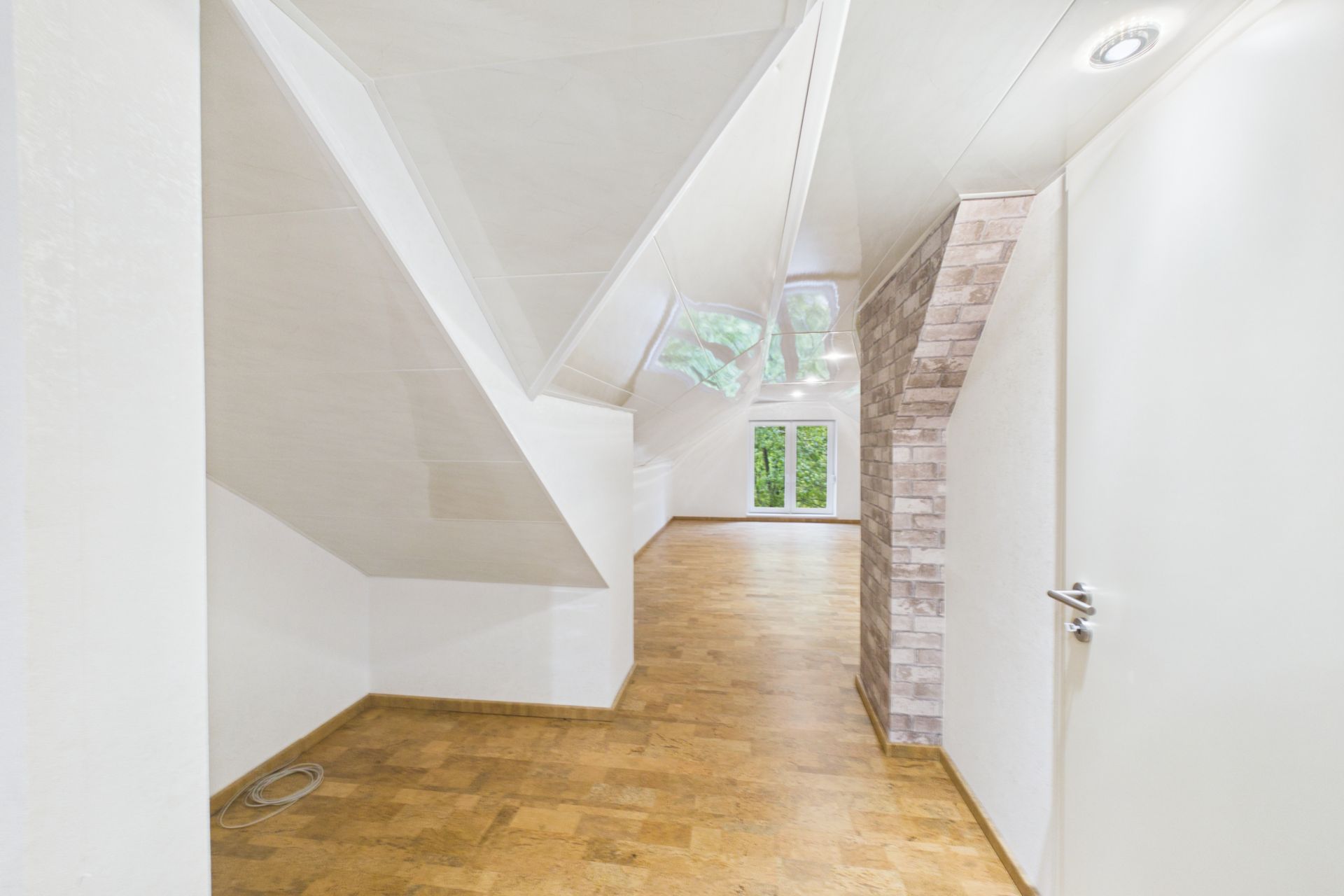 Heller Dachgeschossraum mit schrägen Wänden, Holzboden und großen Fenstern im Hintergrund.