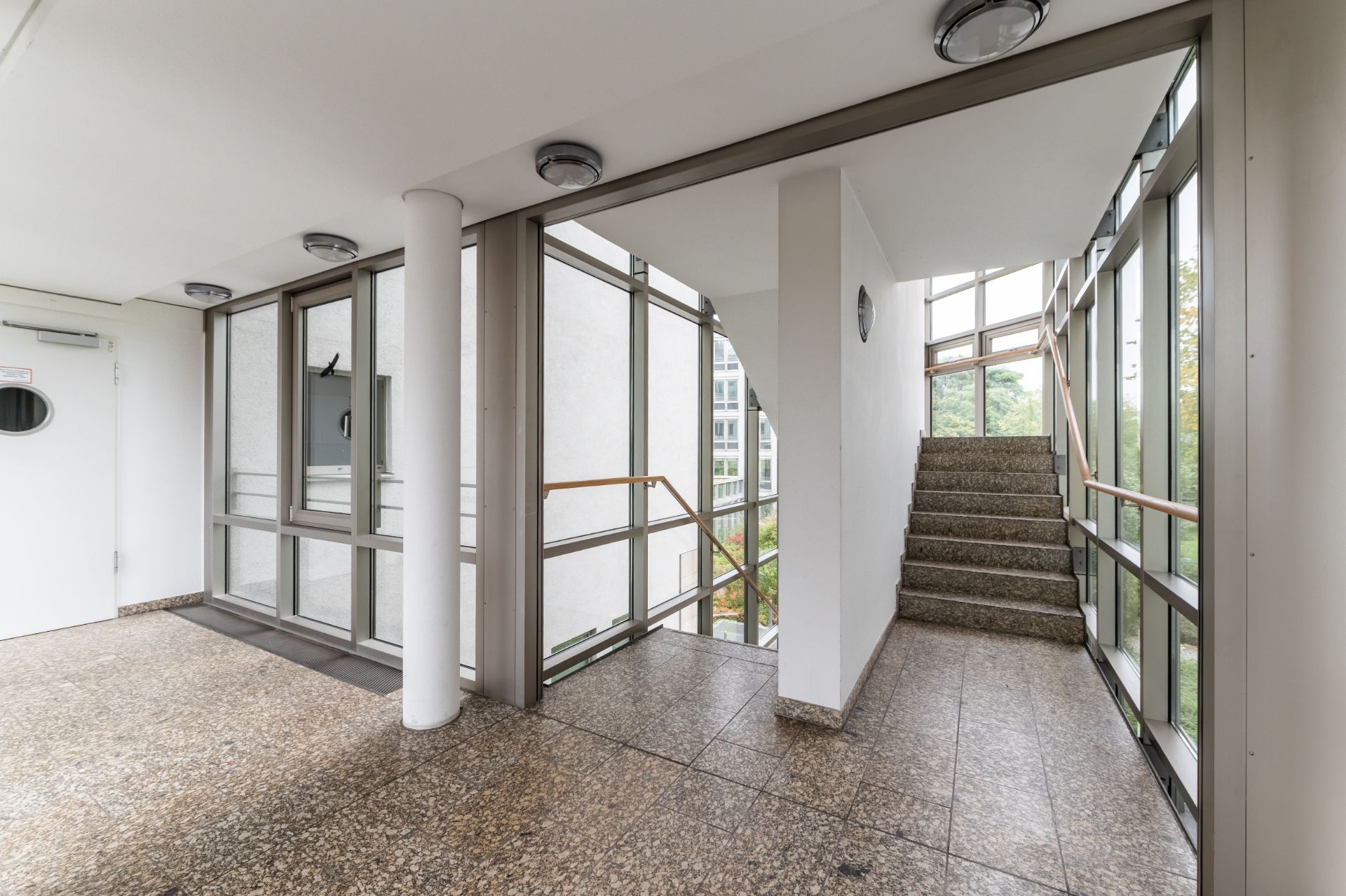 Heller Treppenhausbereich mit großen Fenstern und Treppe in einem Wohngebäude.