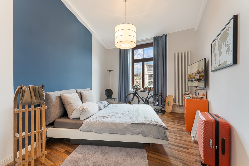 Modernes Schlafzimmer mit Doppelbett, großem Fenster, Fahrrad und rotem Koffer.