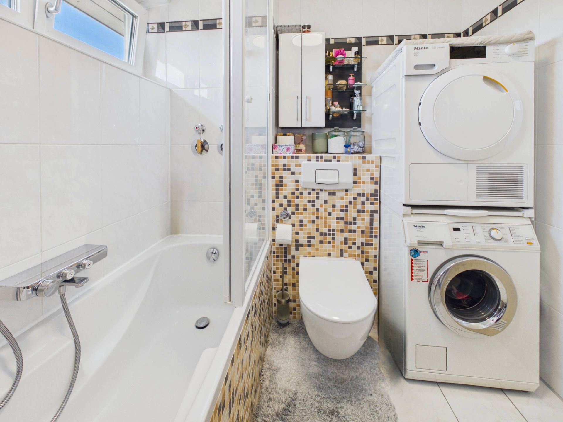 Modernes Bad mit Badewanne, Toilette, Waschmaschine und Trockner, Fliesen in Mosaikoptik.