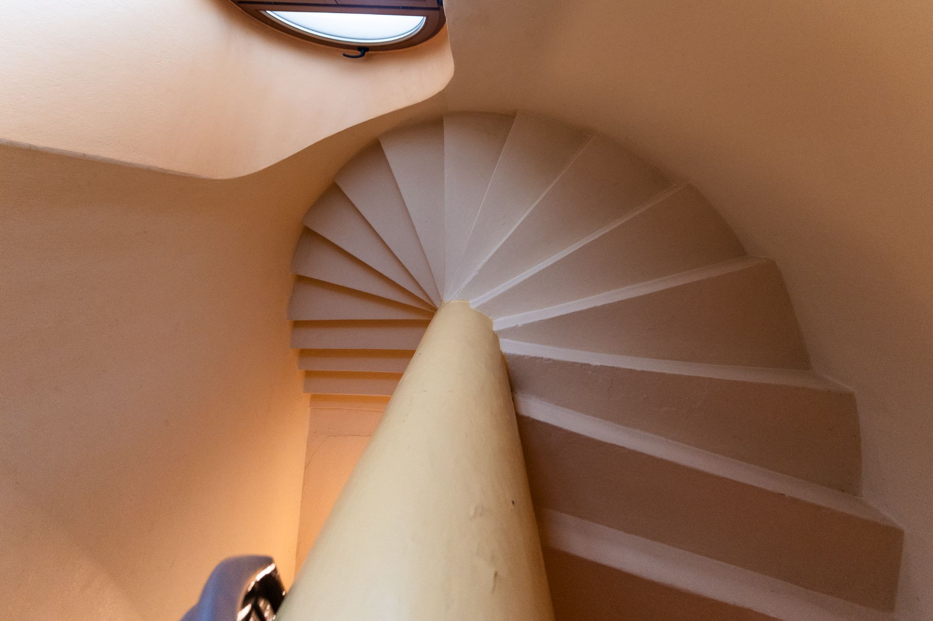 Eine enge, spiralförmige Treppe mit cremefarbenen Wänden und Oberlicht.