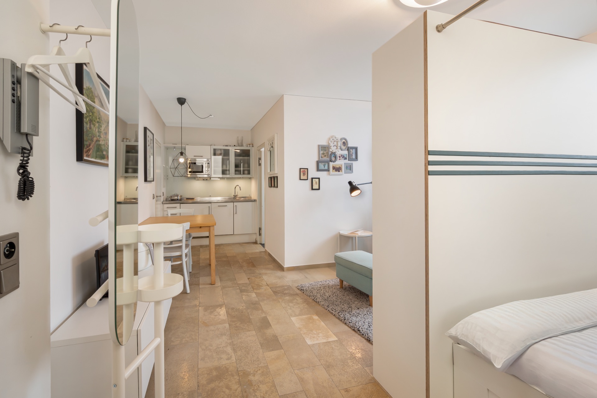 Helles Apartment mit Küchenzeile, Esstisch, Sofa und teilweise sichtbarem Bett.
