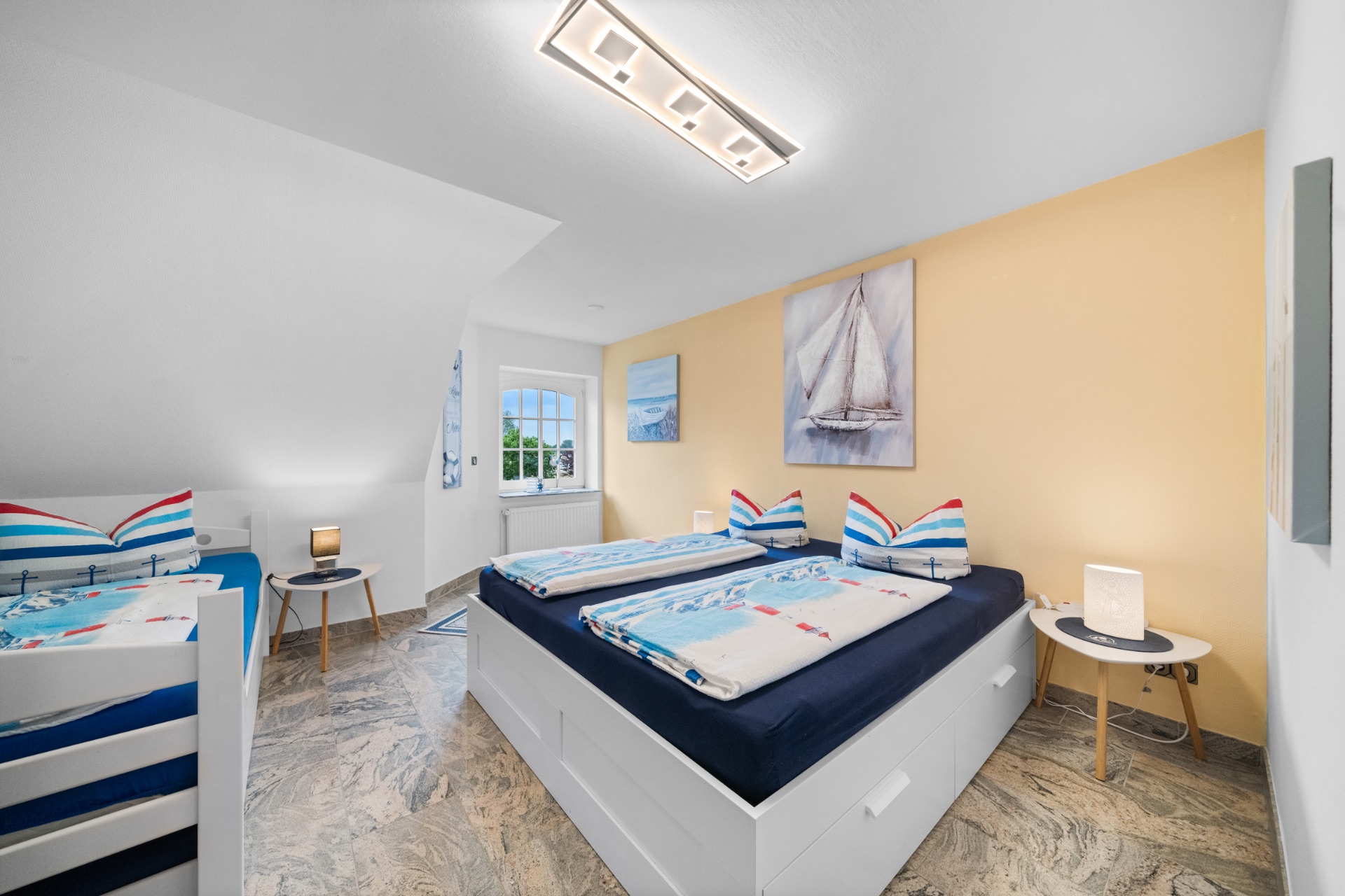 Helles Schlafzimmer mit Doppelbett, Etagenbett, zwei Nachttischen und maritimer Dekoration.