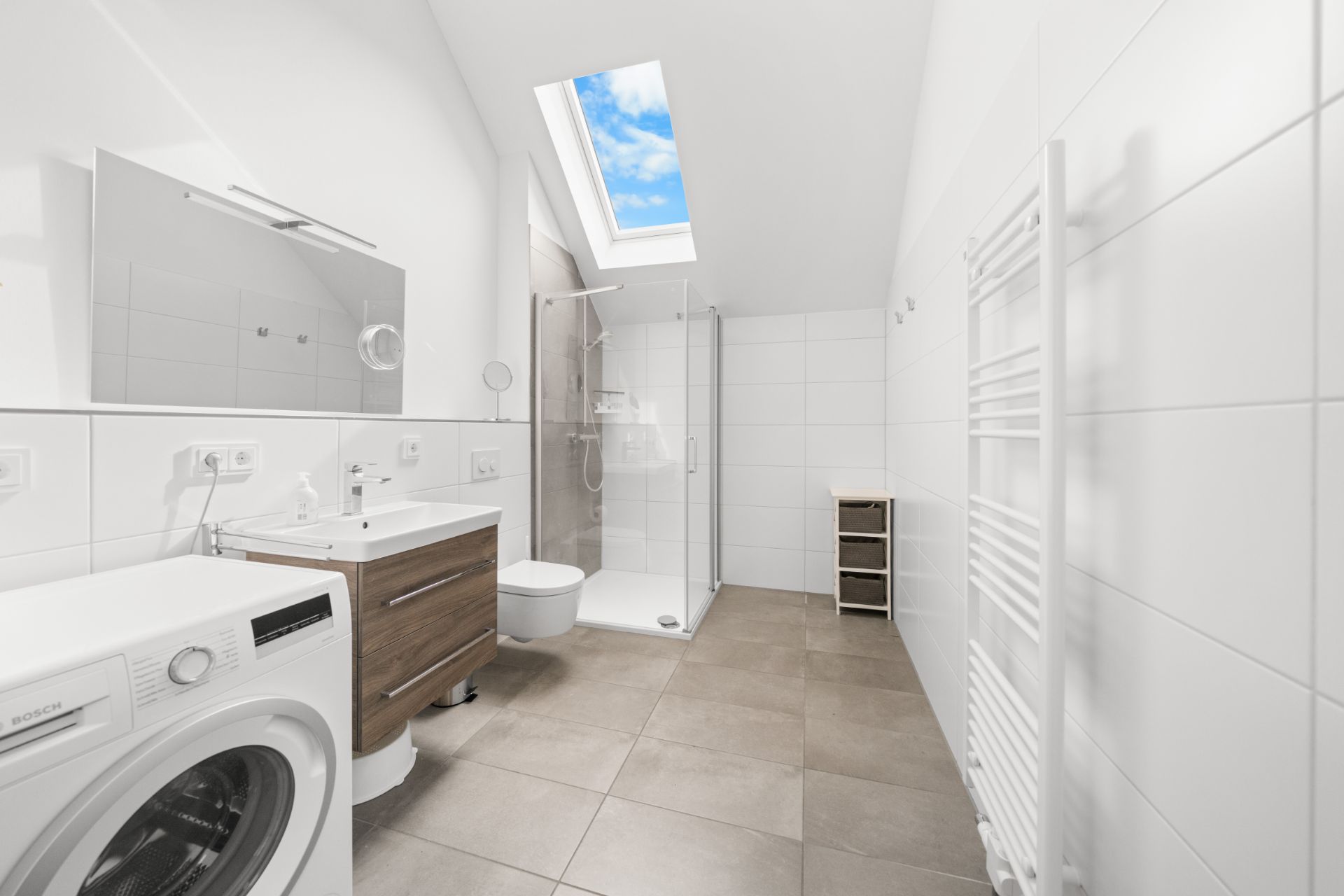Modernes Badezimmer mit Waschmaschine, Dusche, WC, Waschtisch und Dachfenster.