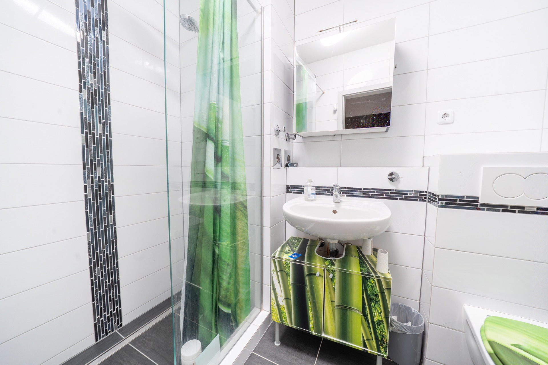 Modernes Badezimmer mit Dusche, Waschbecken, Spiegel und grünen Details.